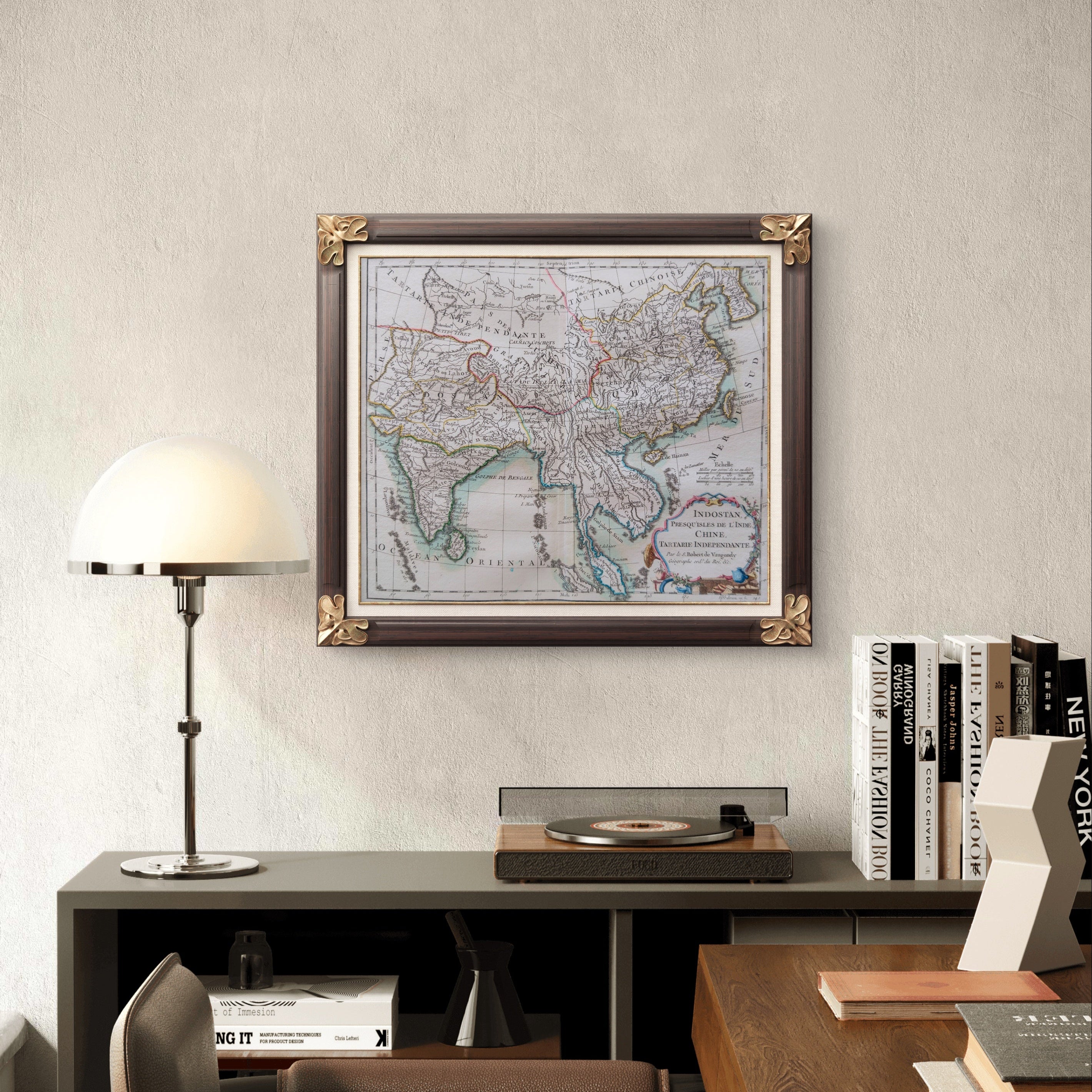 Framed world map on a wall above a desk with books and a lamp.